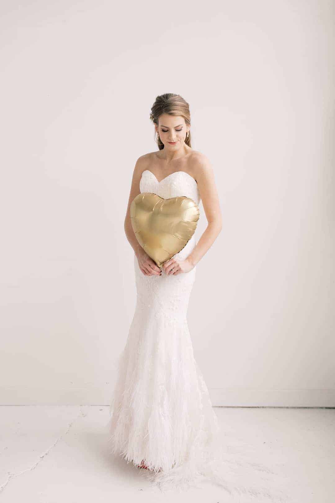 Valentines Day wedding inspiration, featuring giant heart balloon backdrop and romantic feather wedding dress