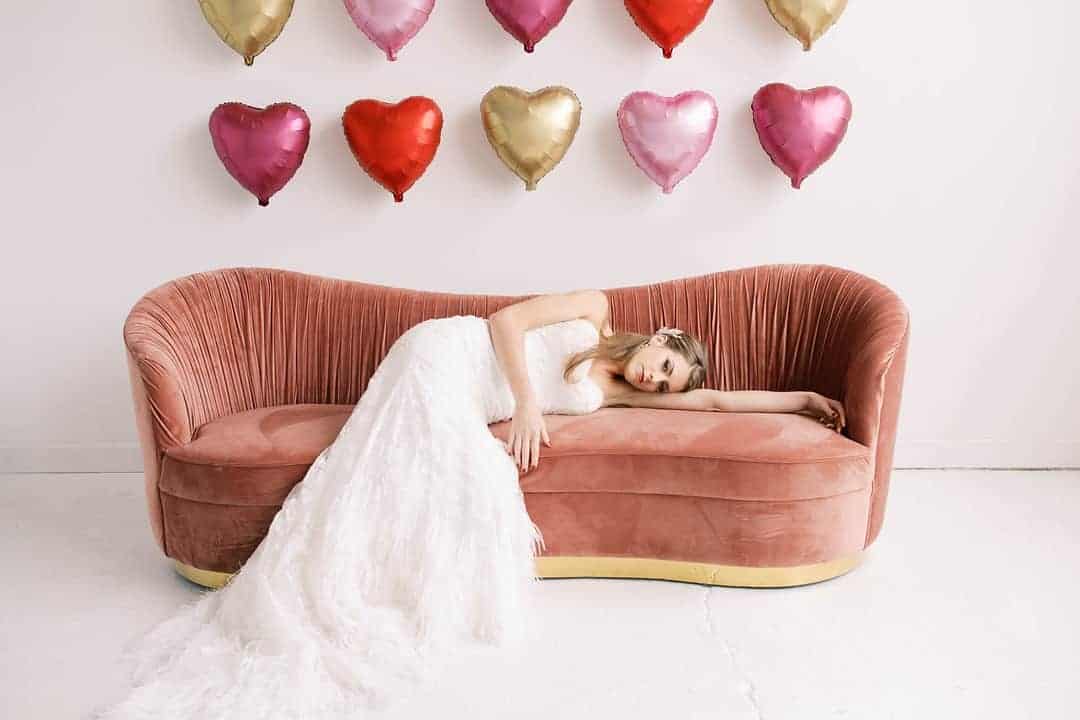 Valentines Day wedding inspiration, featuring giant heart balloon backdrop and romantic feather wedding dress
